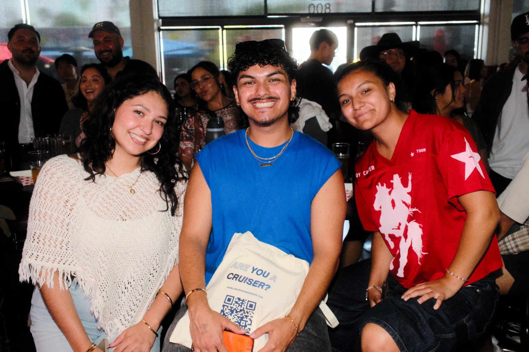 Three friends posing with an "Are You A Cruiser?" tote bag